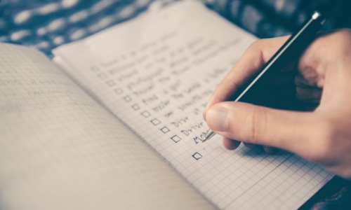 person writing a checklist in a notebook